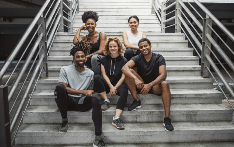 Multi ethnic group of young  people exercise outdoor. They are wearing sport clothing, sitting on stairs and posing for photo